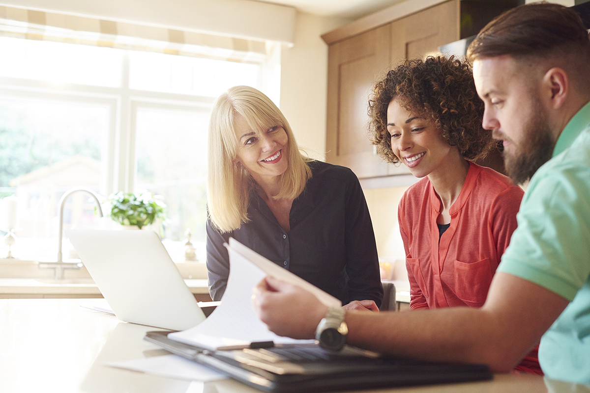 a couple sit in the kitchen of a show home and discuss some figures with the estate agent or mortgage advisor